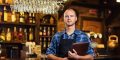 Barman at work in pub,Portrait of cheerful barman worker standing,Waiter giving menus,A pub.Bar.Restaurant.Classic.Evening.European restaurant.European bar.American restaurant.American bar.