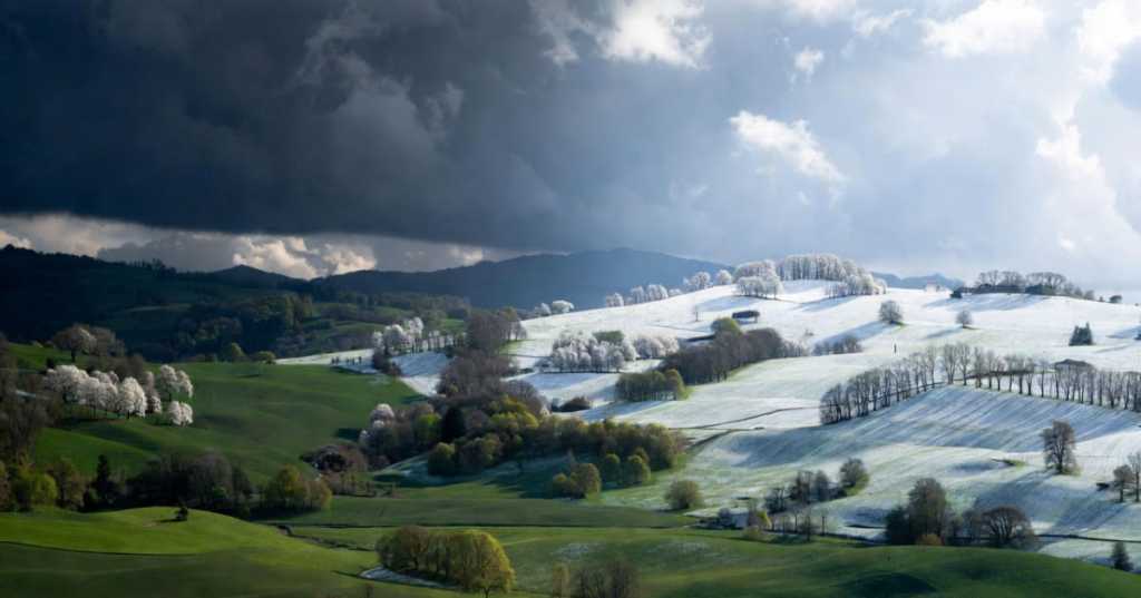 Paesaggio dell’Appennino con alberi in fiore coperti di neve e cielo diviso tra maltempo e schiarite