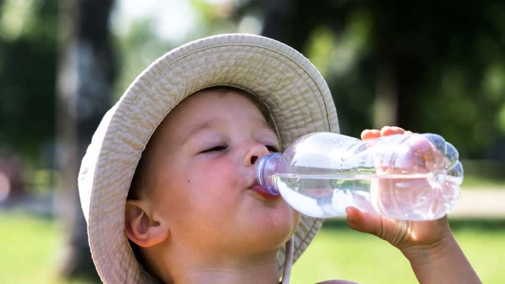 Bambino che beve acqua d'estate per prevenire la disidratazione