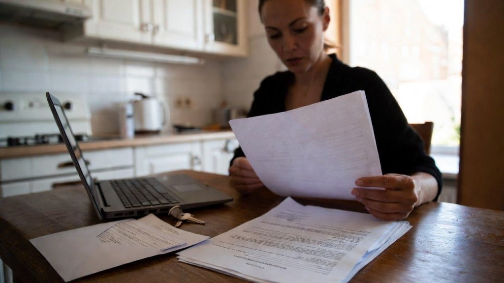 Persona controlla documenti e un contratto di affitto al tavolo di casa con un laptop